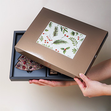 Ein Set von ChocoPostcard Maxi Milk Pralinen in einem festlichen Arrangement mit Ihrem eigenen Foto in der Hand