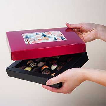 Ein Set mit 20 Pralinen in einer roten Verpackung mit Ihrem eigenen Foto auf Ihren Händen präsentier