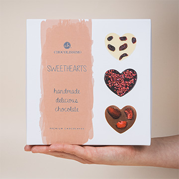 Eine dekorative, herzförmige Schachtel mit belgischen Schokoladenverzierungen, die in der Hand präsentiert wird