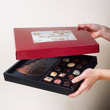 Dekorativ verpackte Weihnachts-ChocoPostcard Maxi rot in der Hand präsentiert