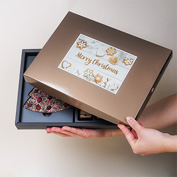 Ein Set von ChocoPostcard Maxi Milk Pralinen in einem festlichen Arrangement mit Ihrem eigenen Foto in der Hand